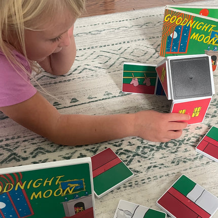 Child playing with 'Goodnight Moon' book and matching cards on a patterned surface