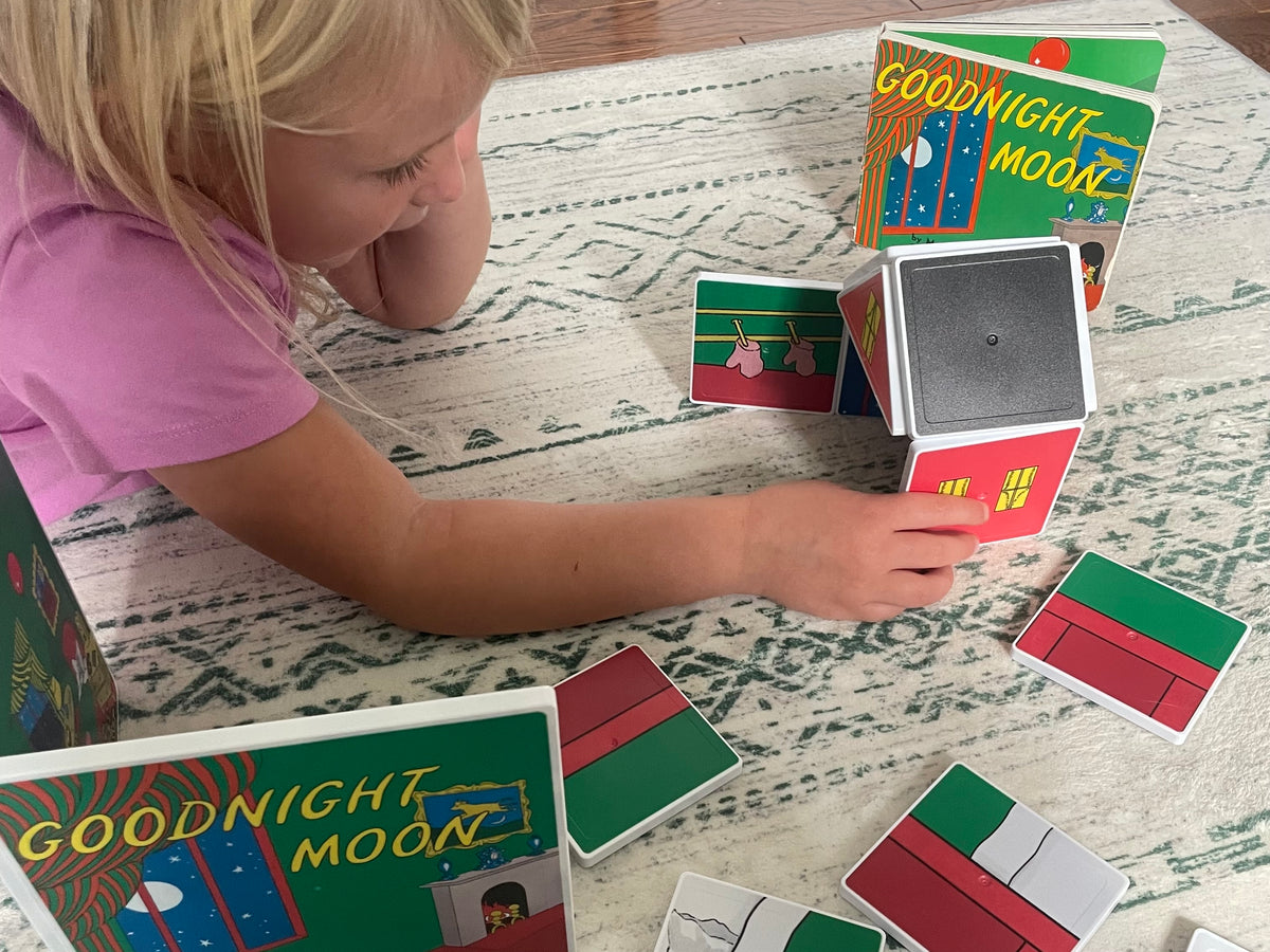 Child playing with 'Goodnight Moon' book and matching cards on a patterned surface