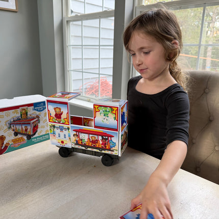 Child playing with a magnetic toy train set on a table, with toy boxes in the background.