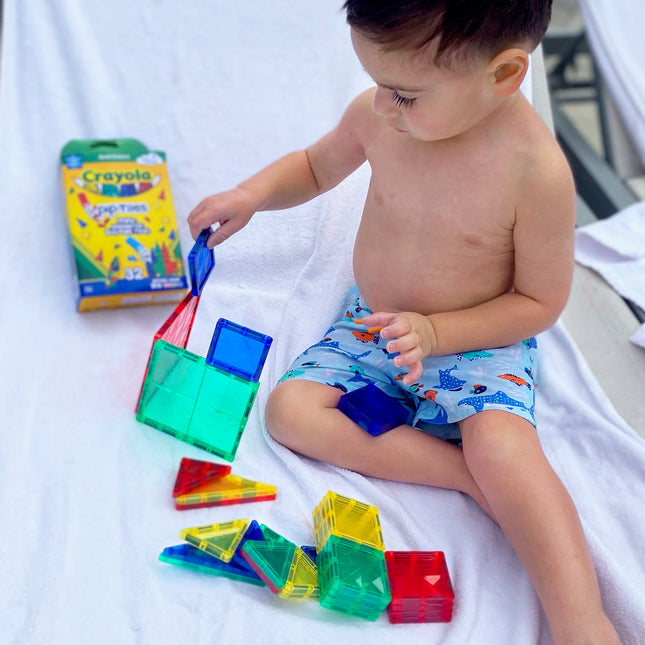 Child playing with colorful magnetic tiles on a white blanket, with a Crayola box in the background.