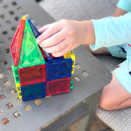 Child playing with colorful magnetic building tiles on a metal surface.
